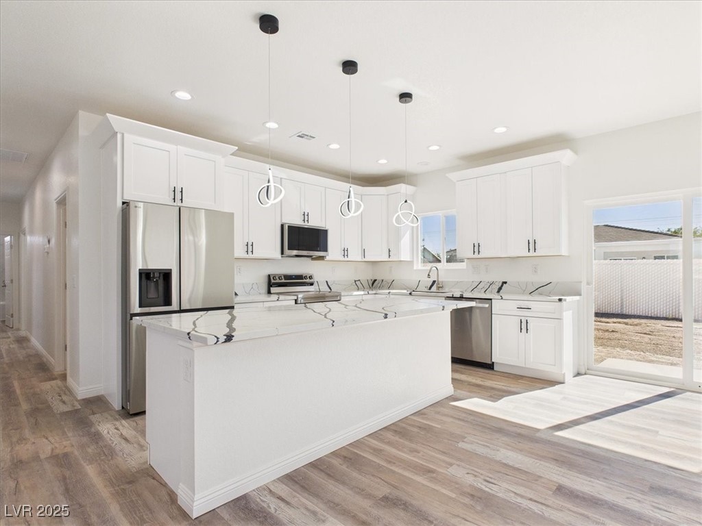 Kitchen featuring appliances with stainless steel finishes, light stone counters, a kitchen island, decorative light fixtures, and white cabinets