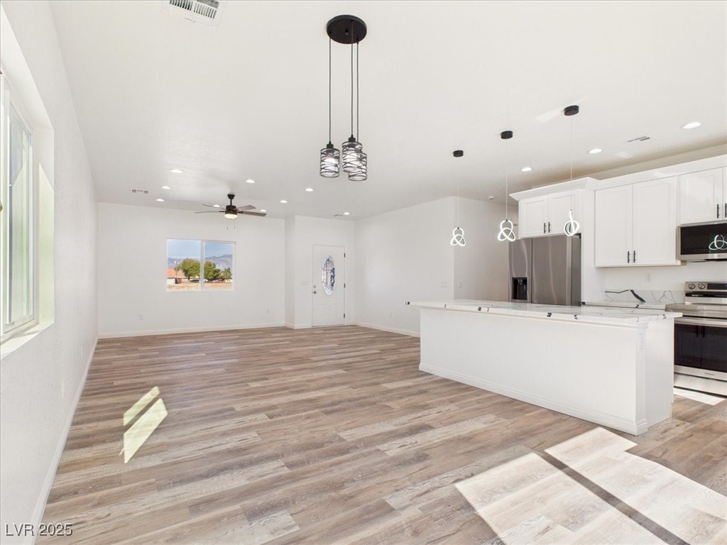 931 Lone Pine Road Pahrump, NV 89048 - Photo 48 of 48 Kitchen featuring white cabinets, decorative light fixtures, appliances with stainless steel finishes, open floor plan, and light wood finished floors