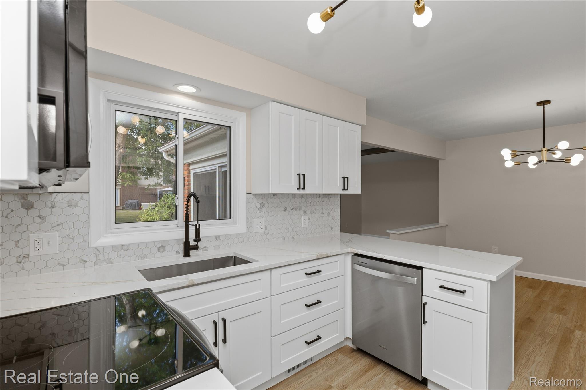 25695 Branchaster Road Farmington, MI 48336 - Photo 13 of 58 White cabinetry, stainless steel dishwasher, hexagonal tile backsplash, light wood-finish flooring, and a contemporary chandelier