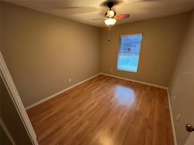an empty room with wooden floor fan and window