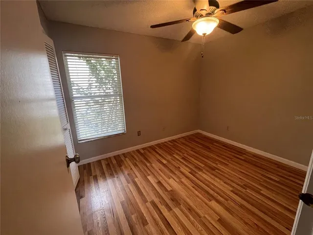 an empty room with wooden floor fan and windows