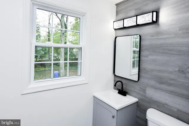 a bathroom with a toilet sink and mirror next to a window
