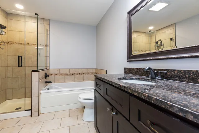 a bathroom with a granite countertop bathtub sink vanity mirror and toilet