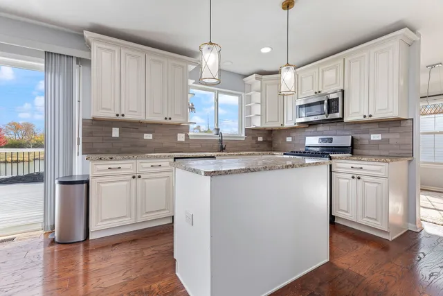 a kitchen with stainless steel appliances granite countertop a sink a stove a refrigerator and white cabinets with wooden floor