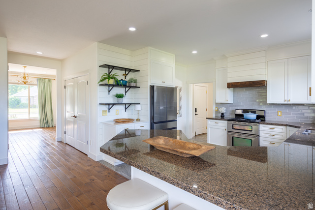 868 Braddock Lane Alpine, UT 84004 - Photo 14 of 64 Kitchen featuring an expansive island with a granite-style countertop, stainless steel appliances, white cabinetry with gold-tone hardware, a subway tile backsplash, and wood-finish flooring