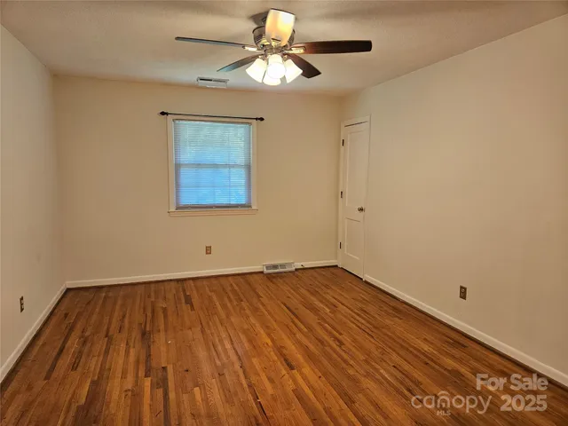 a view of an empty room with chandelier fan and wooden floor