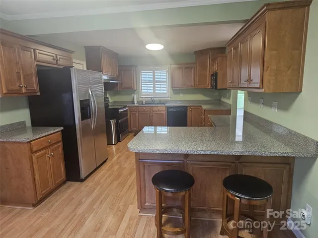 a kitchen with stainless steel appliances granite countertop a refrigerator a stove a sink dishwasher and wooden cabinets with wooden floor