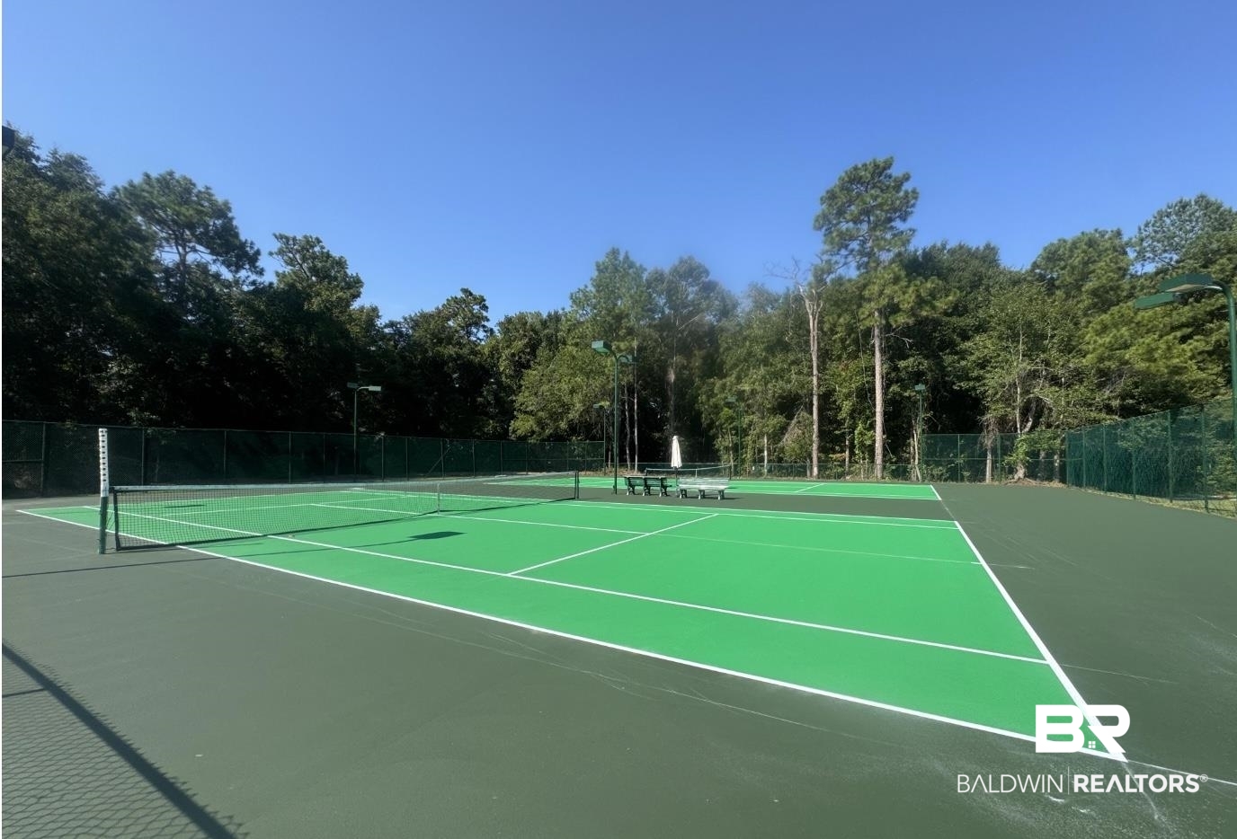 8137 Pine Run Daphne, AL 36527 - Photo 61 of 67 Tennis court featuring a bright green playing surface with white lines, surrounded by a dark green perimeter, tall perimeter fencing, and mature trees