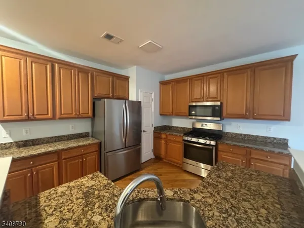 a kitchen with granite countertop wooden cabinets a stove a refrigerator and a sink
