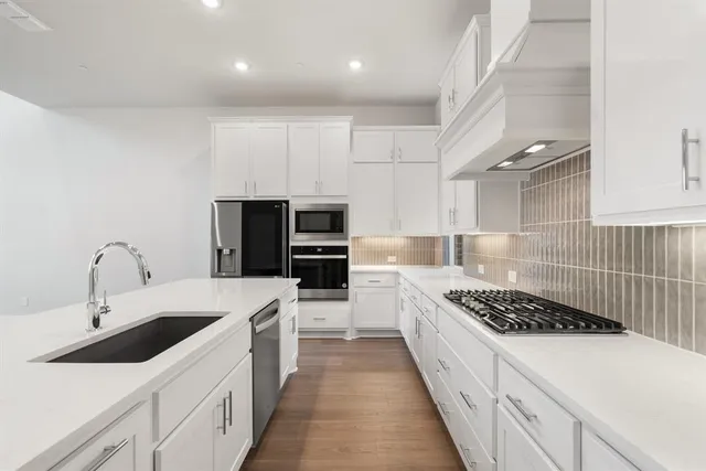 a kitchen with stainless steel appliances a sink dishwasher stove refrigerator and white cabinets with wooden floor