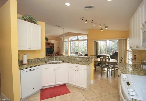 a large white kitchen with granite countertop a stove a sink a dining table and chairs