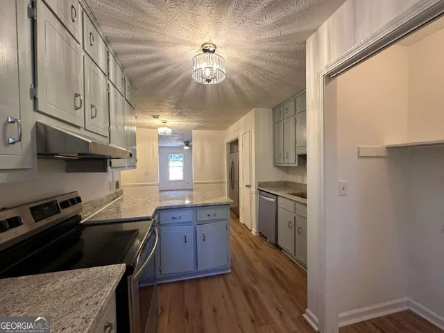 a kitchen with stainless steel appliances granite countertop a refrigerator a sink dishwasher a stove and white countertops with wooden floor