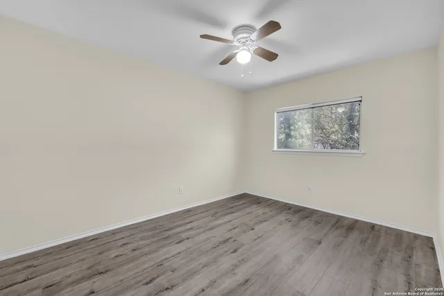 a view of an empty room with wooden floor and a ceiling fan