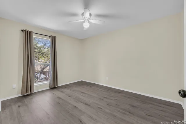 an empty room with wooden floor chandelier fan and windows