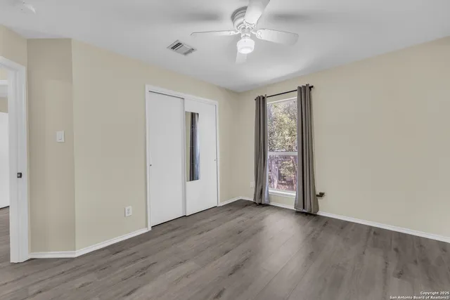 an empty room with wooden floor chandelier fan and windows