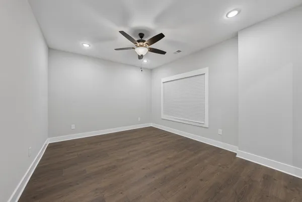 an empty room with wooden floor ceiling fan and windows