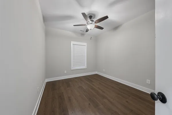 an empty room with wooden floor fan and windows