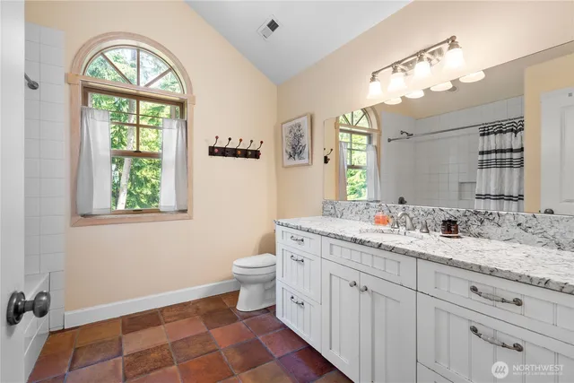 a bathroom with a granite countertop toilet a sink a mirror and a window