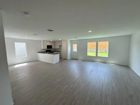a view of a kitchen and an empty room with wooden floor and a kitchen