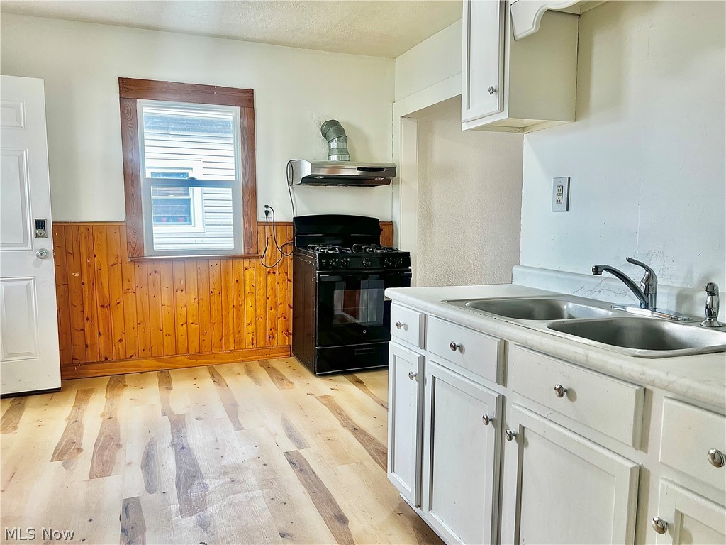 67 Forbes Road Bedford, OH 44146 - Photo 8 of 20 Kitchen with a wainscoted wall, black gas range, wooden walls, light countertops, and light wood finished floors