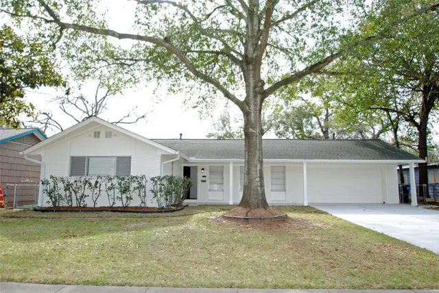 a view of a white house next to a yard and a large tree