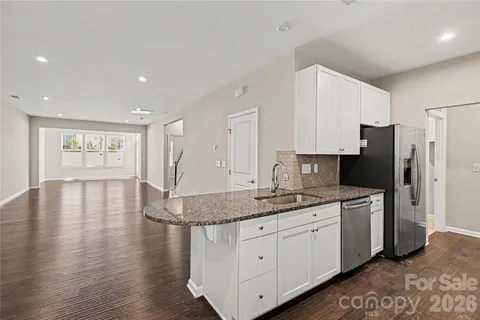 a kitchen with stainless steel appliances granite countertop a refrigerator a sink dishwasher and white cabinets with wooden floor