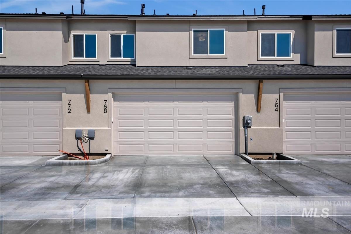 768 South Calhoun Lane Star, ID 83669 - Photo 35 of 36 Stucco exterior featuring multiple garage doors with panel detailing, white-framed windows, and dark shingle roofing