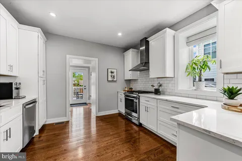 a kitchen with stainless steel appliances white cabinets a stove a sink a potted plant and wooden floor