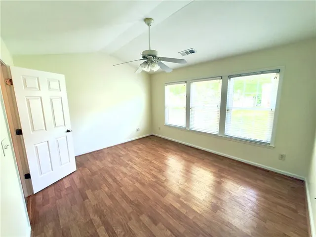 an empty room with wooden floor fan and windows