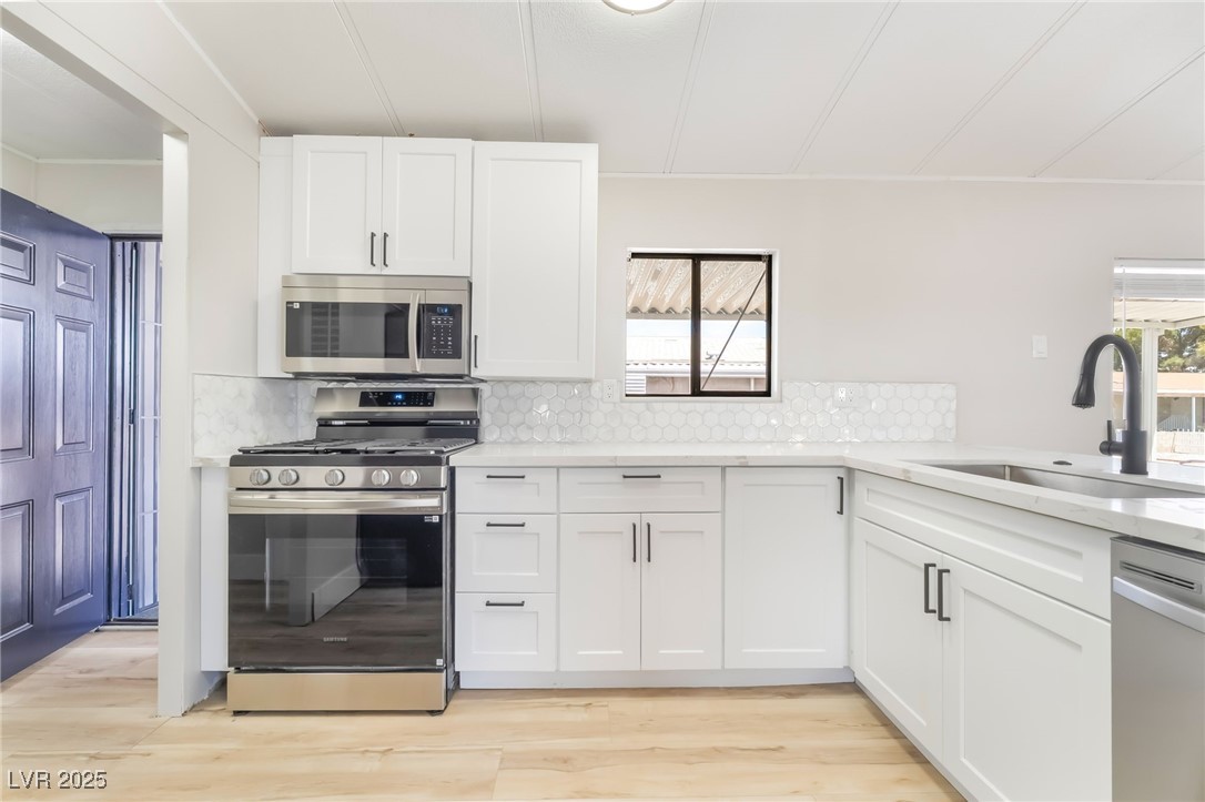 5552 Aldama Road Las Vegas, NV 89122 - Photo 11 of 35 Kitchen with stainless steel appliances, backsplash, white cabinets, and light wood finished floors