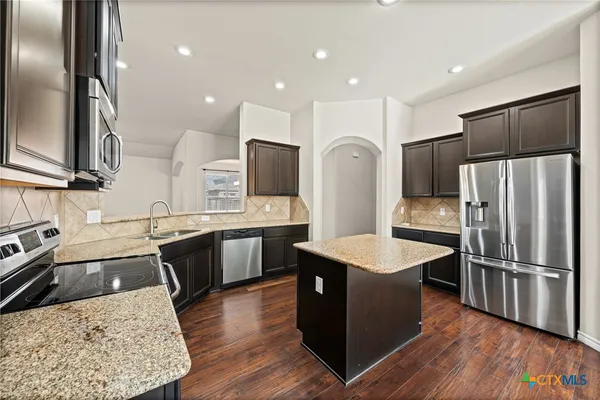 a kitchen with stainless steel appliances granite countertop a refrigerator a sink dishwasher a stove with wooden floors