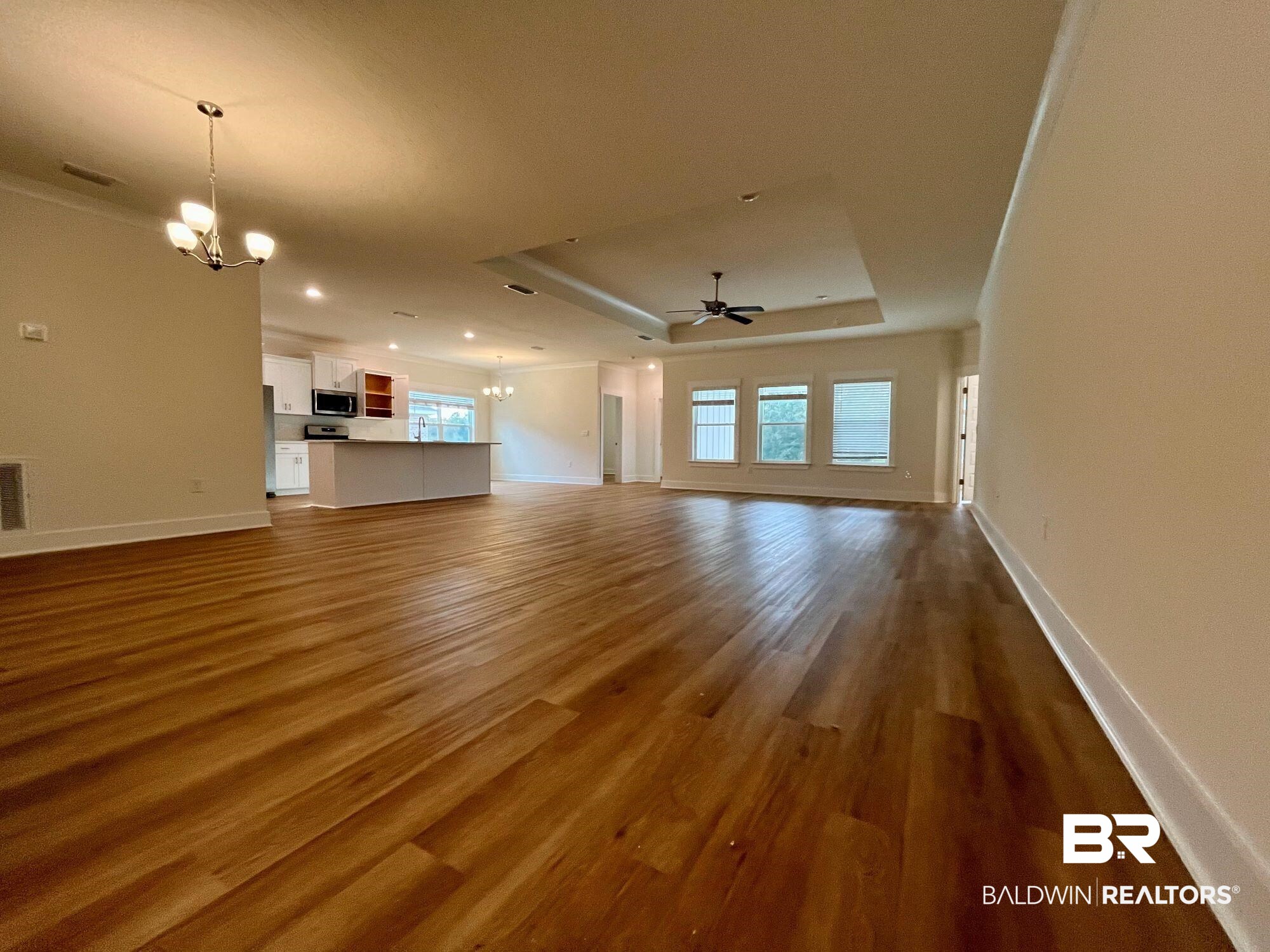 337 Barndling Street Fairhope, AL 36532 - Photo 10 of 34 Unfurnished living room featuring hardwood / wood-style floors, ceiling fan with notable chandelier, a healthy amount of sunlight, and a raised ceiling