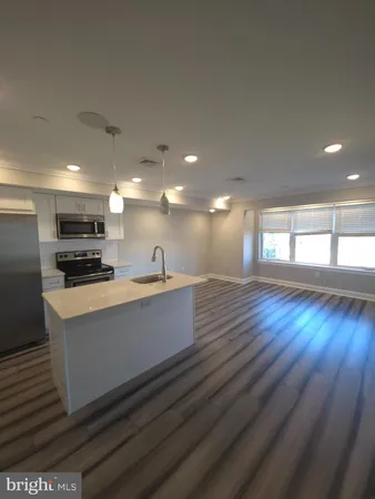 a large white kitchen with kitchen island a sink wooden floor and a refrigerator