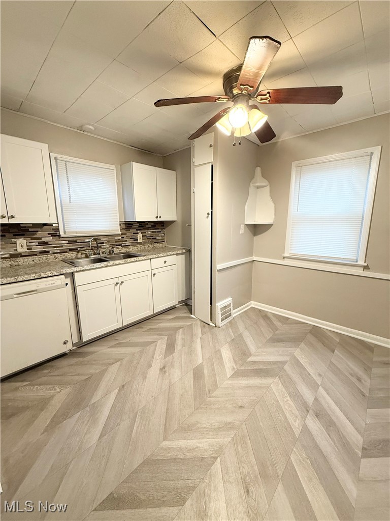 Kitchen featuring white cabinets, dishwasher, a ceiling fan, tasteful backsplash, and light stone countertops