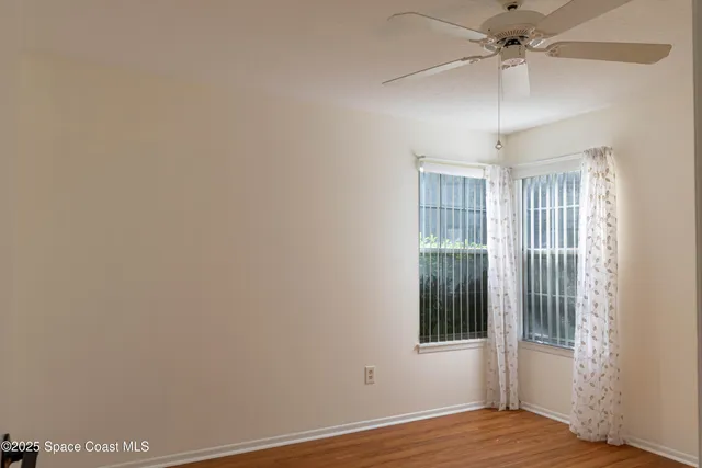 an empty room with wooden floor fan and windows