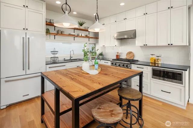 a kitchen with stainless steel appliances granite countertop a stove a refrigerator a microwave a sink and white cabinets with wooden floors