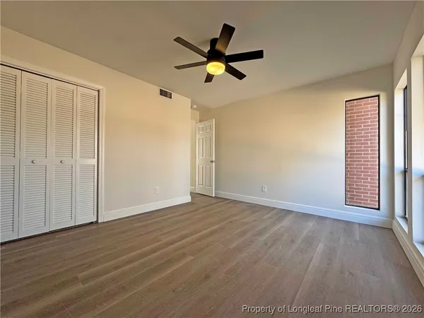 a view of an empty room with wooden floor and a ceiling fan