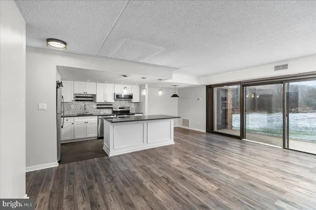 a large kitchen with stainless steel appliances granite countertop a stove a sink dishwasher a refrigerator and white cabinets with wooden floor