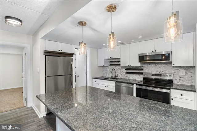 a kitchen with stainless steel appliances granite countertop a sink dishwasher a refrigerator and white cabinets with wooden floor