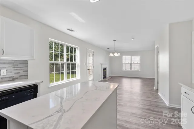 a large white kitchen with granite countertop a stove a sink a refrigerator and white cabinets with wooden floor