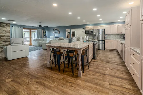 a large kitchen with kitchen island a island a stove a wooden floor and a view of living room