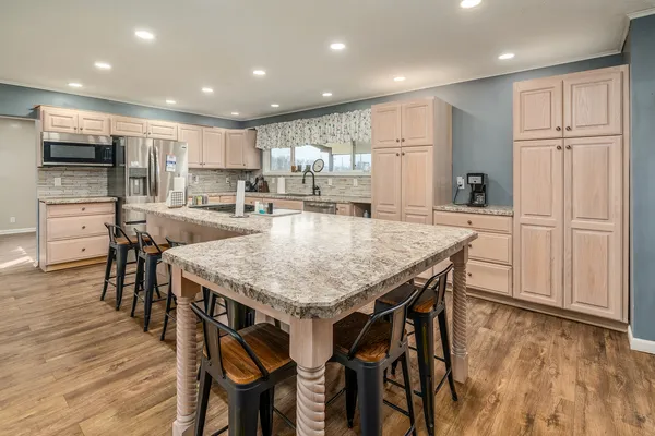 a kitchen with stainless steel appliances kitchen island granite countertop a table chairs refrigerator and microwave