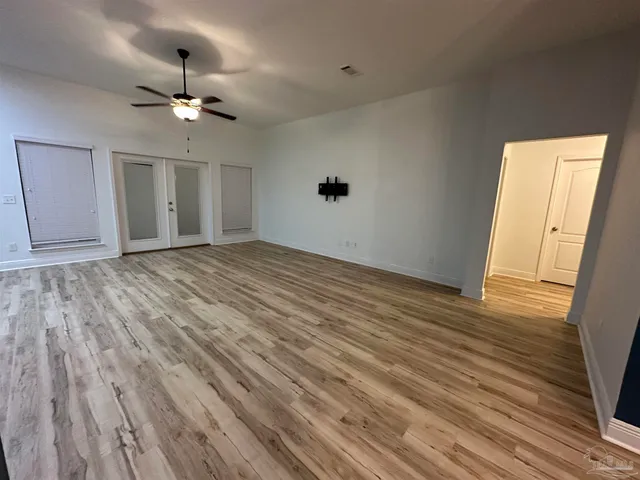 a view of an empty room with wooden floor and a ceiling fan