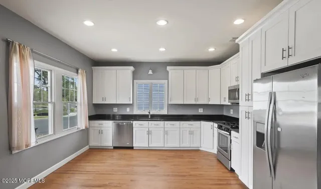 a kitchen with granite countertop a refrigerator a sink and white cabinets