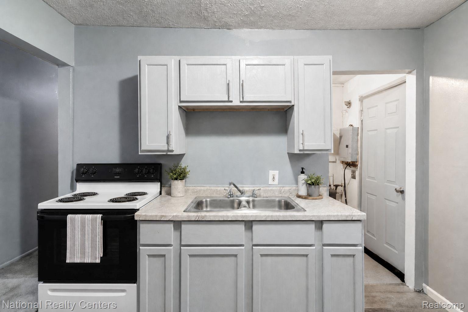 13525 Evergreen Road Detroit, MI 48223 - Photo 9 of 25 Kitchenette featuring light gray cabinetry, a double basin stainless steel sink, and a white electric range