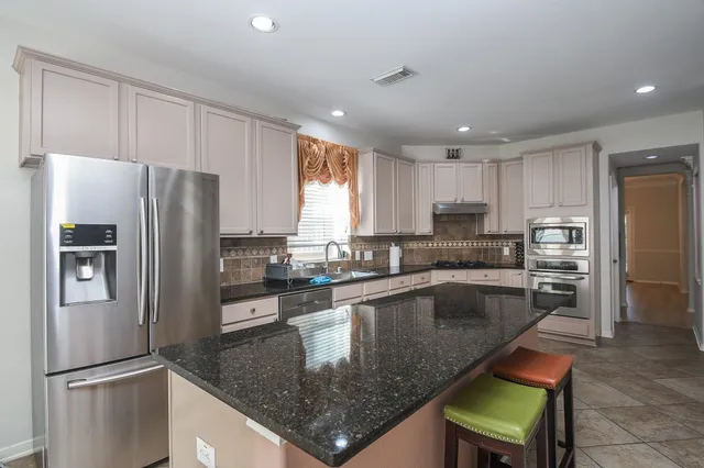 a kitchen with stainless steel appliances granite countertop a refrigerator a stove a sink a dining table and chairs