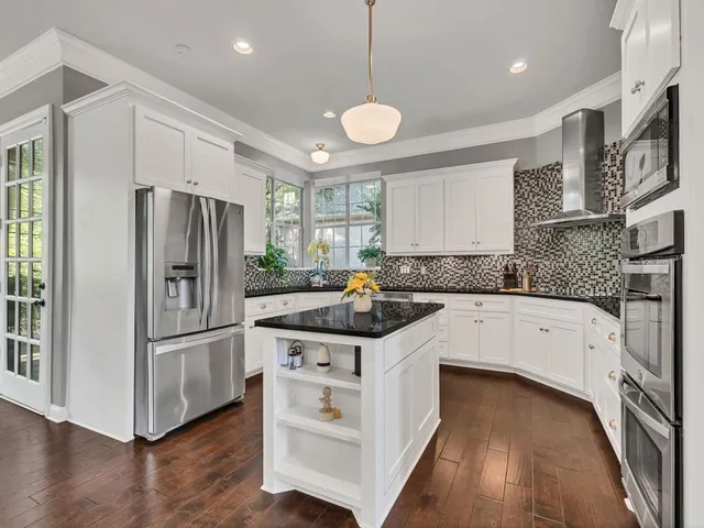 a kitchen with stainless steel appliances granite countertop a refrigerator a oven a sink and white cabinets with wooden floor