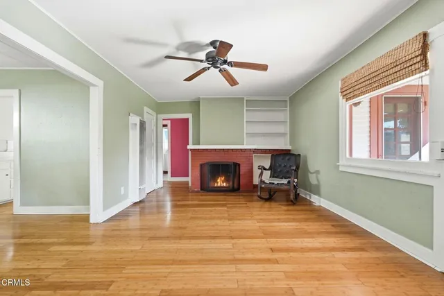 a view of a livingroom with a fireplace a ceiling fan and wooden floor