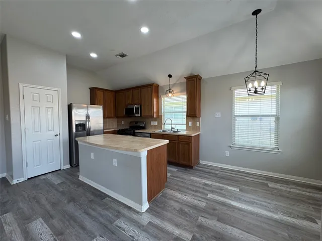 a kitchen with stainless steel appliances granite countertop a refrigerator a sink dishwasher a stove and a dining table with wooden floor