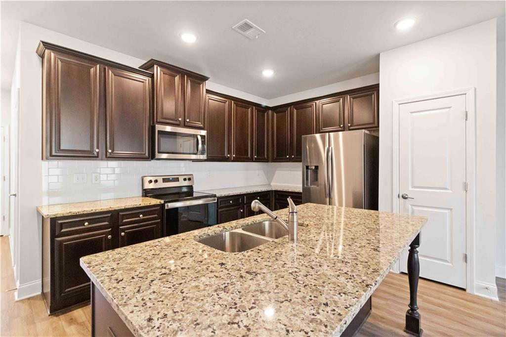 3437 Sumersbe Court Atlanta, GA 30349 - Photo 5 of 25 a kitchen with stainless steel appliances granite countertop a refrigerator a stove top oven a sink dishwasher and wooden cabinets with wooden floor